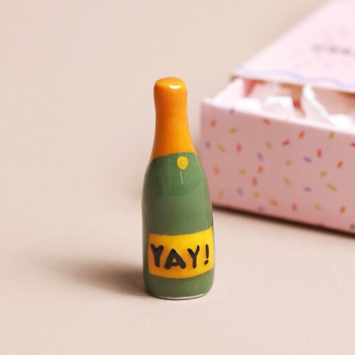 Tiny Matchbox Ceramic Champagne Token  Tiny ceramic Champagne standing on plain surface with the Tiny Matchbox Ceramic Egg Token packaging in background
