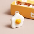 Tiny ceramic egg standing on plain surface with the Tiny Matchbox Ceramic Egg Token packaging in background