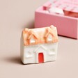 Tiny ceramic House standing on plain surface with the Tiny Matchbox Ceramic Egg Token packaging in background