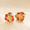 Red Enamel Flower Stud Earrings in Gold on top of beige surface