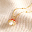 Pearl and Enamel Toadstool Pendant Necklace in Gold laid out on top of beige fabric