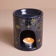 Blue Starry Night Wax Burner with lit tealight in base in front of neutral backdrop