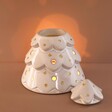 Ceramic Christmas Tree Wax Burner in darkened room with warm light behind and top of wax burner to the side