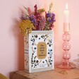 Ceramic Little Book of Flowers Vase on top of wooden counter with lit candle in candle holder and flowers inside