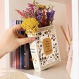 Model placing Ceramic Little Book of Flowers Vase onto book shelf with flowers inside