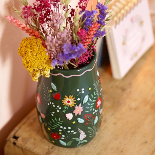 Forest Green Flower Vase on top of wooden counter with flip chart in background in front of beige coloured backdrop