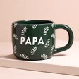 Ceramic Green Leafy Papa Mug on top of raised surface with beige background