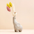 Tiny Elephant Bud Vase with stems inside in front of beige coloured backdrop