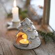 White Ceramic Christmas Tree Tealight Holder in lifestyle shot on top of wooden counter with lit pillar candle in background