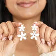 Model smiling holding Pearlescent Acrylic Flower Drop Earrings in front