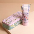 Flower of Focus Power Through Shea Butter Hand Cream Tin Closed with Hand Cream Stood Next To Tin on Beige Surface