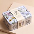 In The Garden Vegan Hand Care and Essentials Tin in Packaging Sleeve on Beige Surface