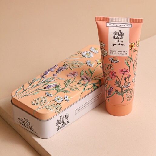 Product Out of Tin In The Garden Shea Butter Hand Cream Stood Next to TIn on Beige Surface