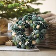 Wooden Green Pinecone Wreath in lifestyle shot leaning on basket