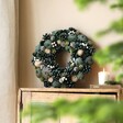 Wooden Green Pinecone Wreath on top of wooden counter with neutral backdrop