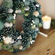 Close up of Wooden Green Pinecone Wreath on top of wooden counter with candle in background