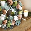 Close up of Wooden Pink and Green Blooms Wreath on top of wooden counter with candle in background