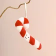 Jellycat Plush Festive Folly Candy Cane Decoration hanging from branch in front of pink background