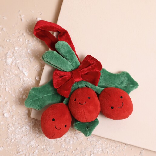 Jellycat Amuseable Holly Soft Toy laid on top of beige coloured surface with fake snow