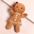 Jellycat Jolly Gingerbread Ruby Soft Toy laid on top of beige coloured background with fake snow
