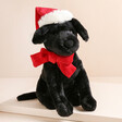 Jellycat Winter Warmer Pippa Black Labrador Soft Toy on top of raised surface in neutral shade