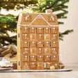 Personalised Wooden Gingerbread House LED Advent Calendar on top of counter with Christmas tree in background