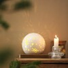 Ceramic LED Celestial Ball Light on top of wooden surface with lit candle beside