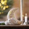 Ceramic LED Celestial Moon Light on top of wooden counter in front of Christmas tree with lit candle to the side