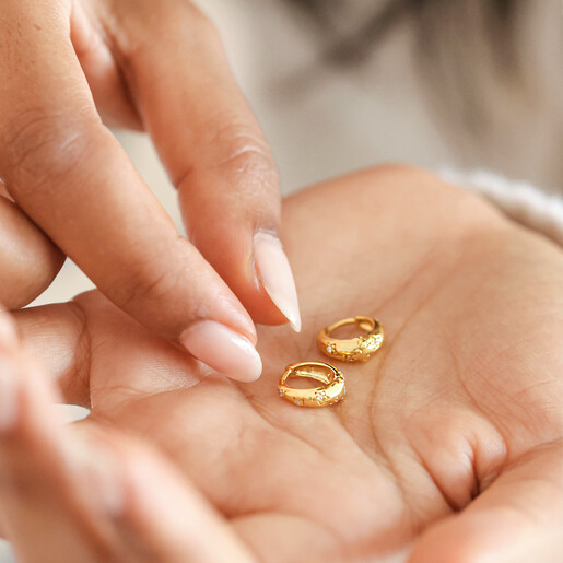 Model holding Crystal Daisy Star Dome Huggie Hoop Earrings in Gold in palm of hand