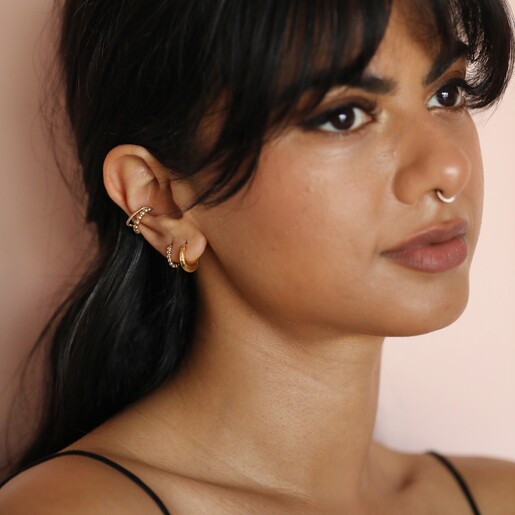 Model wearing Gold Sterling Silver Faceted Dome Huggie Hoop Earrings against beige backdrop