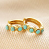 Gold Sterling Silver Teal Stone Huggie Hoop Earrings stacked on top of neutral coloured fabric