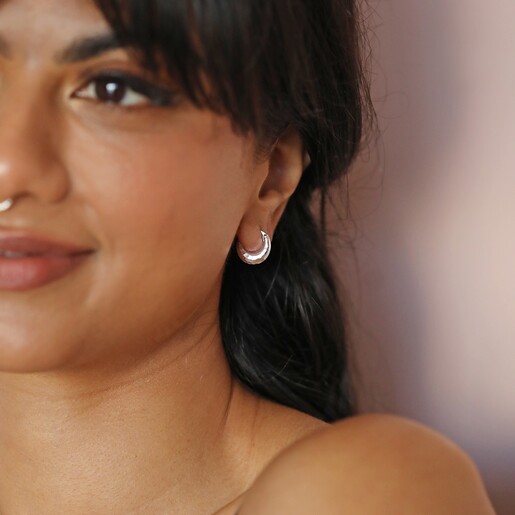 Model smiling wearing Sterling Silver Faceted Dome Huggie Hoop Earrings against beige background