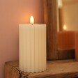 Cream Ribbed Wax LED Pillar Candle Lit in Darkened Room With Mirror Behind 