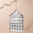 Festive Metal House Advent Calendar hanging from tree branch against natural coloured background
