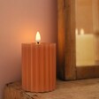 Pink Ribbed Wax LED Pillar Candle in Darkened Room, Lit with Mirror in Background 