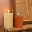 Pink and Cream Ribbed Wax LED Pillar Candle Lit in Darkened Room with Mirror Behind 
