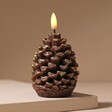 Wax Pinecone LED Candle lit up against pink background