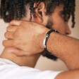 Men's Stainless Steel Feature Braided Leather Bracelet in Black on model with hand behind neck in front of beige coloured material