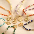 Close up of Crown Chakra Beaded Necklace in Gold with other necklaces on top of beige coloured fabric