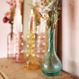 Blue Glass Posy Vase in lifestyle shot on top of wooden counter with bubble candle holders in background