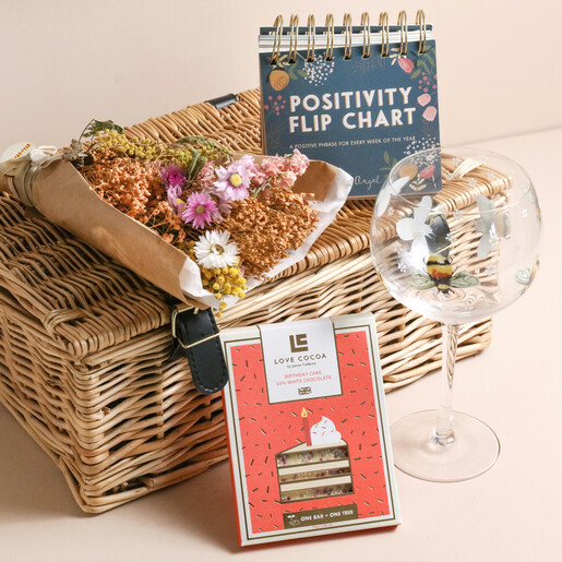 Happy Birthday Floral Wicker Gift Hamper With Products on Top on Beige Background 