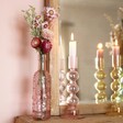 Pink Glass Bottle Vase with flowers inside in lifestyle shot with candle holders in background