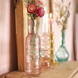 Pink Glass Bottle Vase on top of wooden counter in lifestyle shot with blue vase and candle holders behind