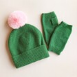 Green and Pink Pom Pom Bobble Hat With Matching Hand Warmers on Beige Surface