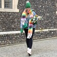 Model walking wearing Personalised Vibrant Rainbow Striped Winter Scarf and holding eucalyptus