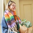 Model smiling wearing Personalised Vibrant Rainbow Striped Winter Scarf and holding eucalyptus