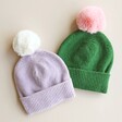 Green and Pink Pom Pom Bobble Hat With Lilac and Cream Pom Pom Bobble Hat on Beige Surface