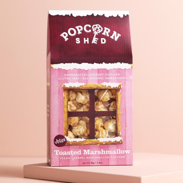 Popcorn Shed Toasted Marshmallow Gourmet Popcorn on top of raised surface with pink backdrop