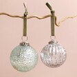 Floral Debossed Mint Green Bauble With Silver Ribbed Glass Bauble Hanging on Pink Background 