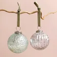Silver Ribbed Glass Bauble with Other Silver Bauble Hanging on Branch on Pink Background 